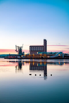 View of the industrial harbor area with a grain silo and crane reflecting in the calm water at sunset in Oslo, Oslo, Norway.