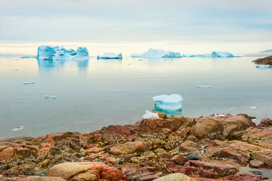 Icebergs near the coast in Saqqaq village, western Greenland. Colorful stones on the sea shore. Summer seascape at sunset
