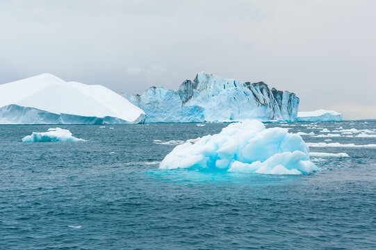 Big icebergs in Atlantic ocean, Ilulissat icefjord, western Greenland. Waves on the sea at windy cloudy day.