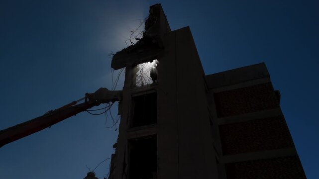 Artistic view of a crane demolishing a multi-story building in sunny weather.