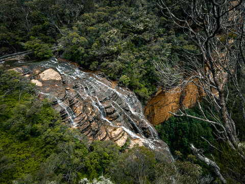 View of the Blue Mountains waterfall cascading over rocky ledges surrounded by lush eucalyptus forest in Katoomba, New South Wales, Australia.