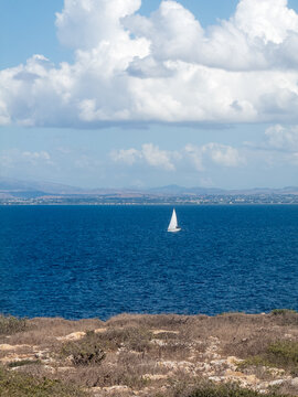 View of a white sailboat on the blue sea near the rocky coastline of the Island of Favignana, Favignana, Sicily, Italy.