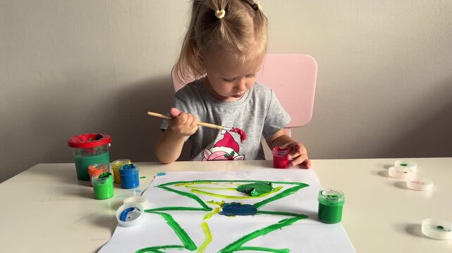 Toddler paints a paper tree using bright colors at a white table, hands on creative learning activity.