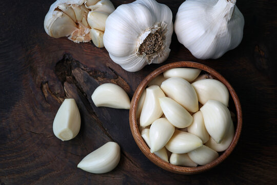 Garlic cloves in a bowl with peeled garlic on wooden background