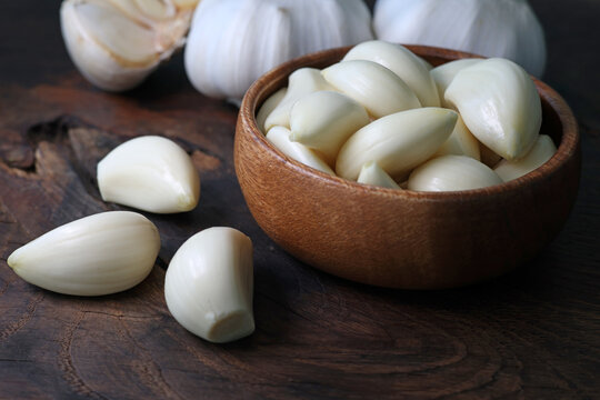 Garlic cloves in a bowl with peeled garlic on wooden background