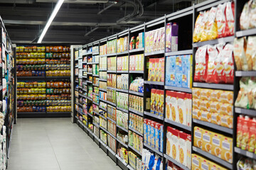 Fototapeta premium Aisle, grocery and food in supermarket for retail shopping, business or consumable supply chain. Empty, row or products with shelves or variety of snacks, inventory or stock for produce or storage