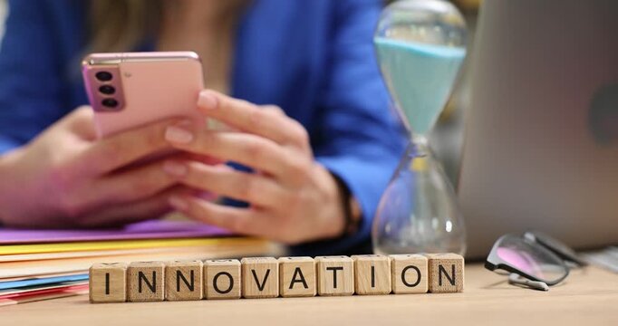 Word Innovation on wooden cubes near hourglass and businesswoman hands holding smartphone. Digital technology for business development integration