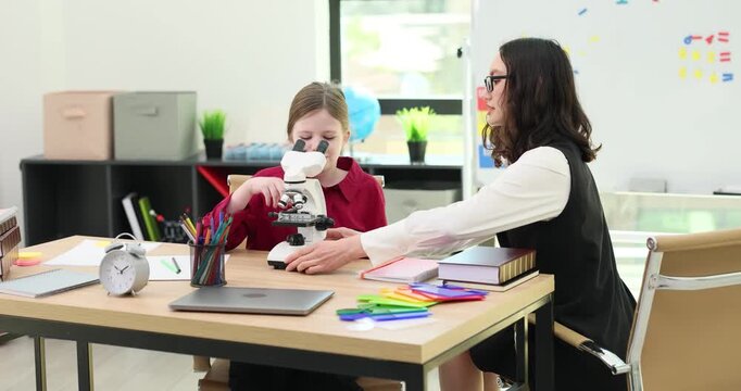 Young teacher shows microscope to smart girl student in home classroom. Tutor helps pupil to learn natural science during private lesson at home
