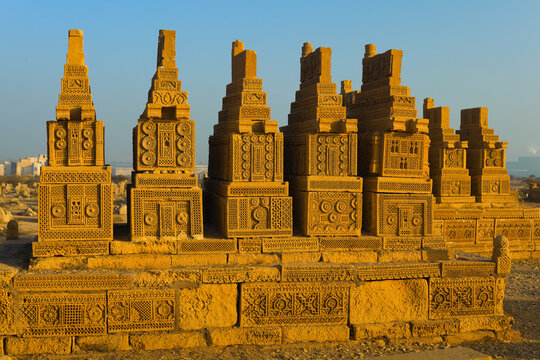 Karachi, Pakistan - 22 January 2010: View of the historic Chaukhandi Tombs featuring intricate sandstone carvings and pyramidal structures under a clear blue sky.