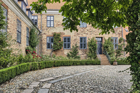 Viborg, Denmark - 07 August 2026: View of the historic courtyard of Viborg Stift with traditional brick architecture, cobblestone ground, and lush greenery in the Latinerhaven garden.