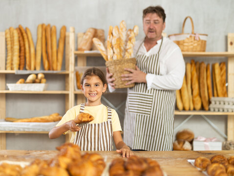 Baker dad and daughter are standing near product range in bakery kitchen.