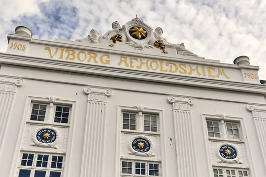 Viborg, Denmark - 07 August 2026: View of the historic Viborg Afholdshiem building featuring a white facade with ornate gold lettering and decorative medallions under a cloudy sky.
