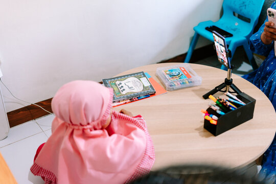 Child learning online at a small round table with books and a smartphone on a tripod