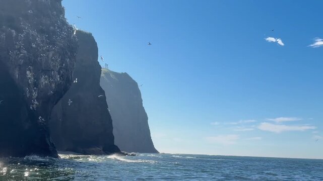 Dramatic cliff face dropping steeply into deep blue sea, rugged maritime landscape, imposing natural scenery.