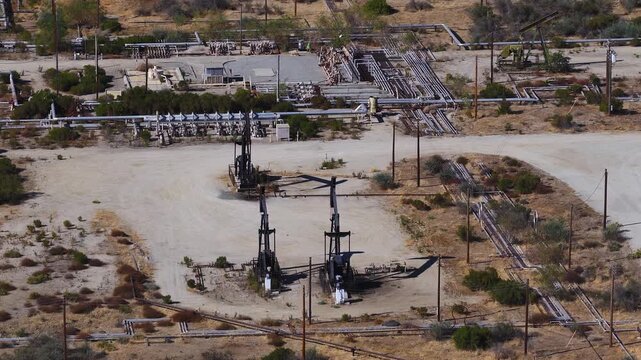 Aerial view of active pump jacks extracting petroleum near pipelines and desert terrain in a California oil field, capturing industrial machinery and fossil fuel energy infrastructure.
