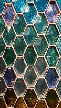 Close-up of a decorative wall made of colorful hexagonal Falconet glass blocks in a honeycomb pattern, featuring shades of blue, green, purple, and amber with textured surfaces.