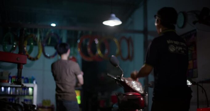 Two mechanics or customers watch football on television while working around a moped in dim repair shop, leaping up with joy triumph punching and celebrations