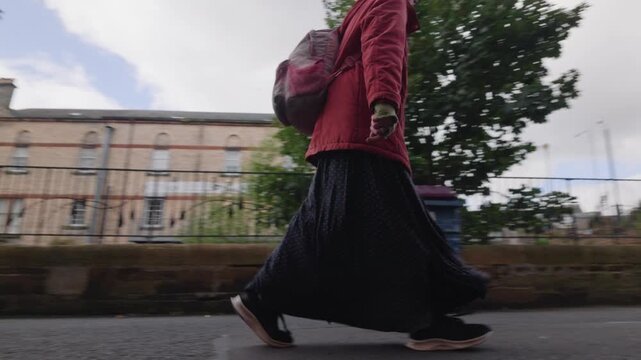 Low-angle tracking, homeless woman walks alone through a quiet deserted part of town, showing homelessness, isolation and everyday urban social issues from a low street level perspective