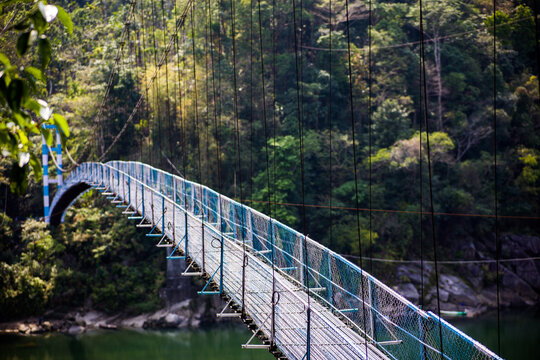 Meghalaya, India - 31 March 2023: View of a suspension bridge spanning a river surrounded by dense forest and lush greenery.