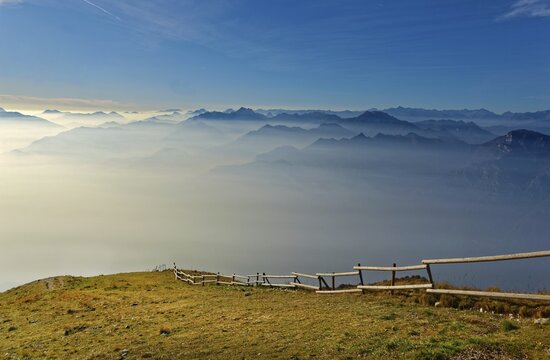 Meadow with fence and Lake Garda in the morning mist with Lake Garda mountains and Bergamo Alps, Monte Baldo, Malcesine, Verona Italy, Trentino-Alto Adige, Italy
