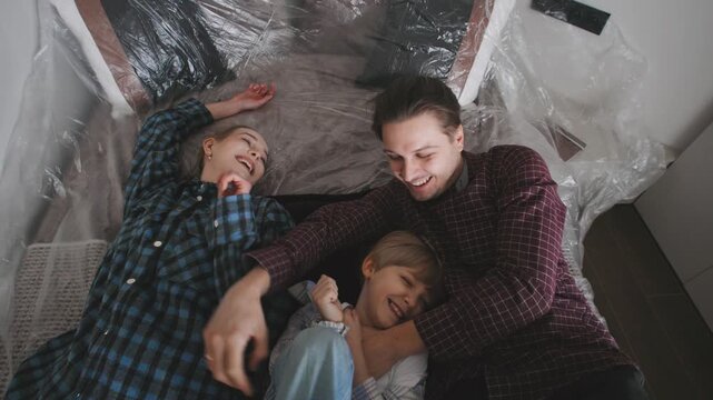 A couple and their son are falling on a bed in their new home. They are moving in with cardboard boxes around them.