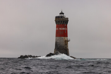 Le phare des Pierres Noires se dresse sur son îlot rocheux au large du Finistère, battu par les vagues de l’Atlantique, avec sa silhouette rouge et blanche caractéristique © Tof - Photographie