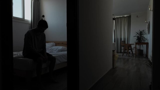 Isolated man enters empty bedroom and sits alone on bed