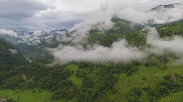 Moody aerial drone view of dramatic layered clouds rolling over a deep green valley with distant peaks in rural Nepal