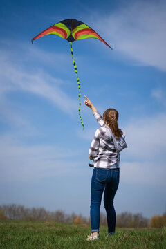 Young woman is flying a colorful kite against a bright blue sky, enjoying a carefree summer day and feeling a sense of freedom, happiness, and recreation outdoors. Vertical photo