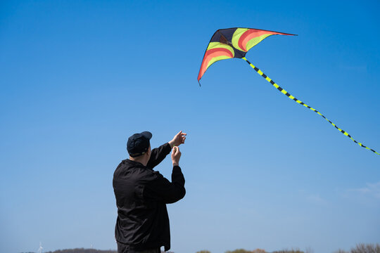 Man controls a colorful kite soaring against a clear blue sky, enjoying sunny outdoor leisure in a park - playful, relaxed summer activity capturing freedom and joy