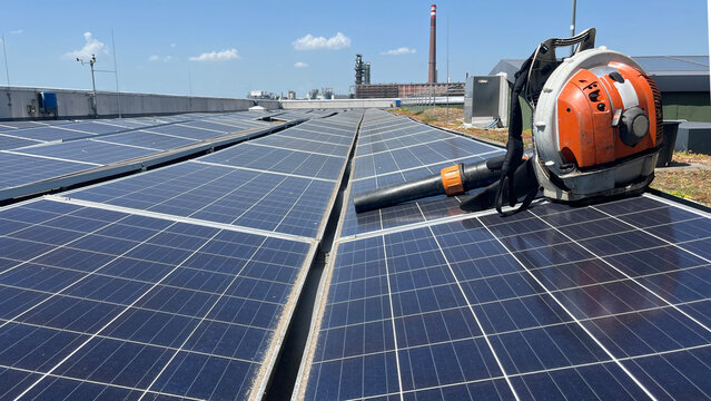 Solar panels on a rooftop with a leaf blower positioned on the panel, for maintenance and cleaning content, renewable energy infrastructure upkeep, space for text