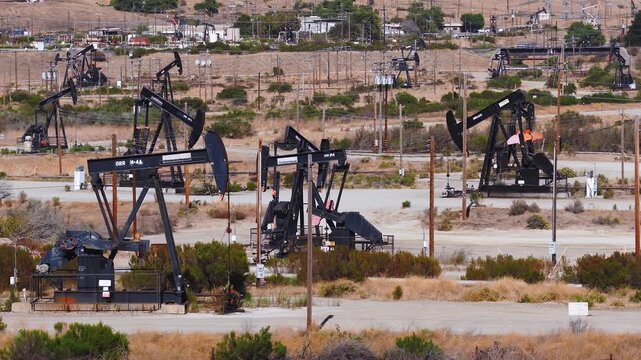 Aerial shot captures numerous mechanical pump jacks pumping petroleum continuously across an arid California oil field landscape, highlighting industrial energy infrastructure and extraction.
