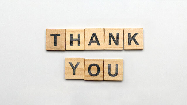 Wooden letter tiles forming the words THANK YOU on a light gray background, top view flat lay concept expressing gratitude. Thank You Message