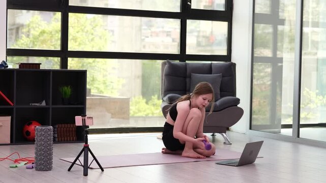 Teenage girl in comfortable sportswear performs dumbbell workout. Child uses smartphone to create engaging fitness tutorial for imaginary audience