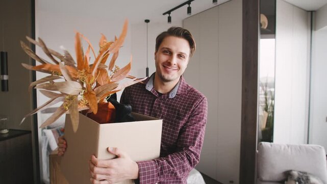 A man holds a cardboard box filled with plants and decorative items. Boxes are scattered around the house.