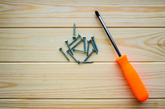 Carpentry works background. A screwdriver with an orange handle and a pile of metal screws on the light pine planks, flat lay