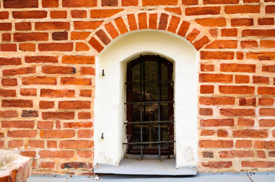 Historic architecture background. An arched window with black metal bars in a red brick wall. White plaster framing around the opening and weathered brickwork