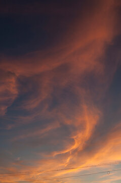 Dramatic sky background. Dark clouds lit by warm golden sunlight at sunset. Soft streaks across the sky and thin power lines along the lower edge of the frame