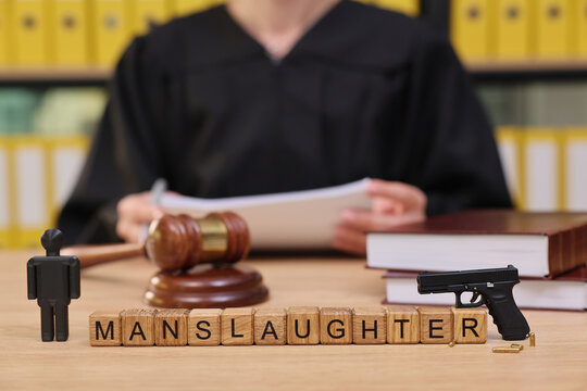In a courtroom, a judge prepares to address a case involving manslaughter. A gavel, a small figure, and a toy gun sit on the table, highlighting the gravity of the situation.