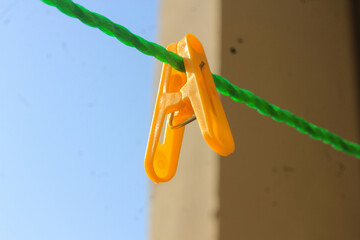 Bright yellow plastic clothespin hanging securely on a vivid green rope against a soft blurred background © Rehman