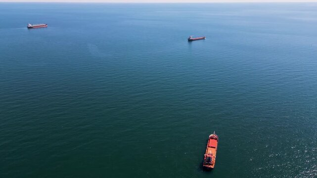 Aerial view of cargo ships and tankers anchored in open calm blue sea waters