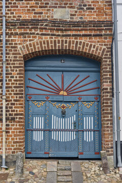 Ribe, Denmark - 20 July 2026: View of an ornate blue wooden door with intricate carvings, a sunburst motif, and a lion head knocker set into a historic brick wall in the old town.