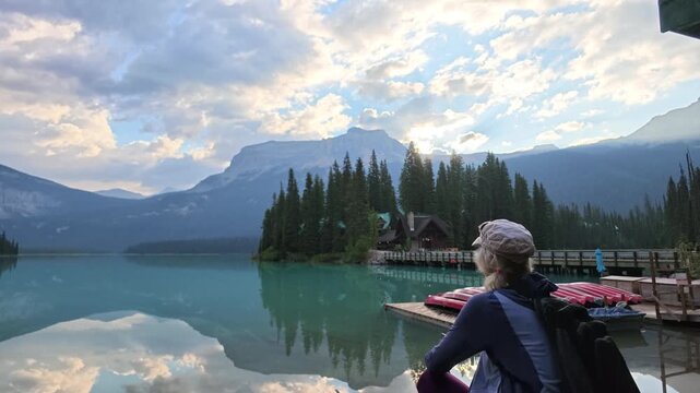 top view of woman by turquoise waters of Emerald Lake,admiring reflections of mountains and clouds,with boat dock and red canoes, enjoying summer travel in Yoho National Park, British Columbia, Canada