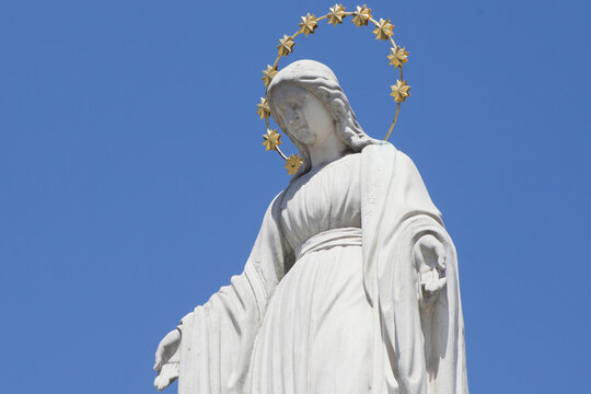 Statue of the Virgin Mary with a golden halo against a clear blue sky, symbol of faith, maternal love, hope, purity and divine protection.