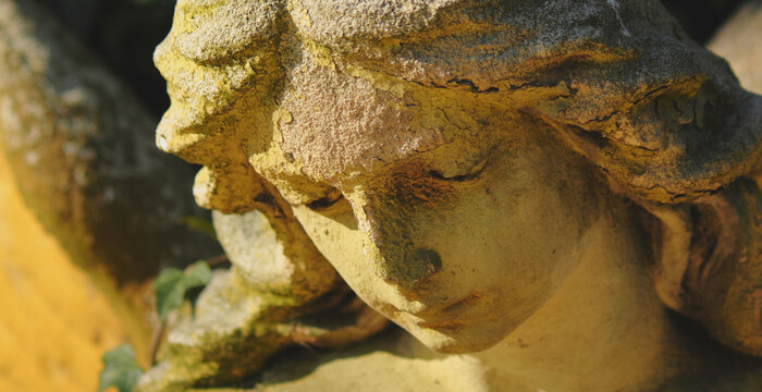 Close-up of an old weathered angel statue with a sorrowful face, symbolizing grief, compassion, empathy, mourning and remembrance.
