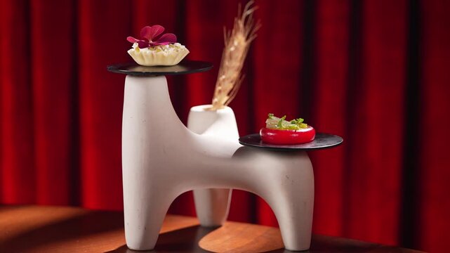Gourmet appetizer served on a unique sculptural stand against a rich red velvet curtain backdrop