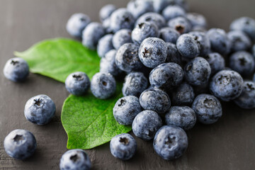 Fresh ripe blueberries with green leaves arranged on a dark textured surface, showcasing their vibrant color and natural appearance. © tai