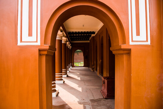Dhaka, Bangladesh - 21 January 2022: View of the historic arched corridors and columns of Lalbagh Fort, featuring vibrant orange-red walls and intricate architectural details.