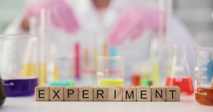 Word Experiment spelled with wooden cubes against flasks with colored liquids. Scientific research of fluid properties by professional in lab