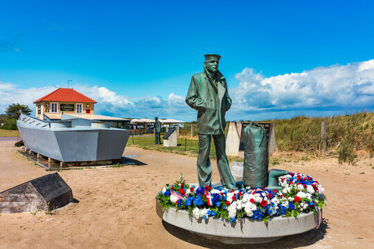 Utah Beach, Normandy, France - 10 June 2026: View of the US Navy monument at Utah Beach, featuring a bronze sailor statue with floral tributes and a landing craft replica on the sand.